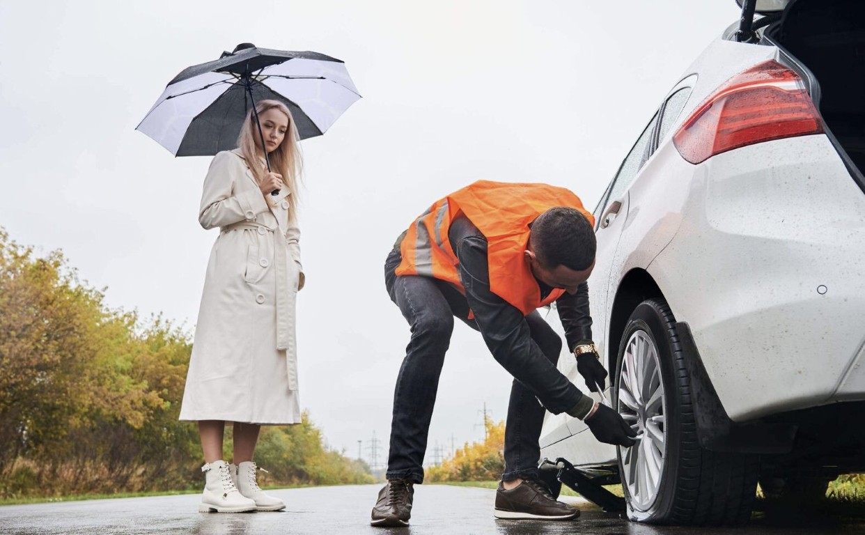 Professional roadside assistance technician helping stranded driver in rain